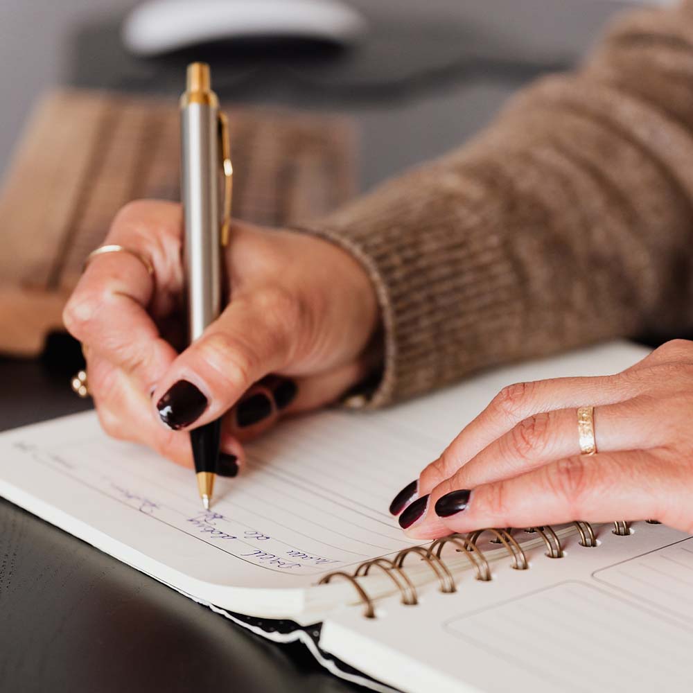 Photo d'une personne écrivant sur un cahier avec un stylo en aluminium