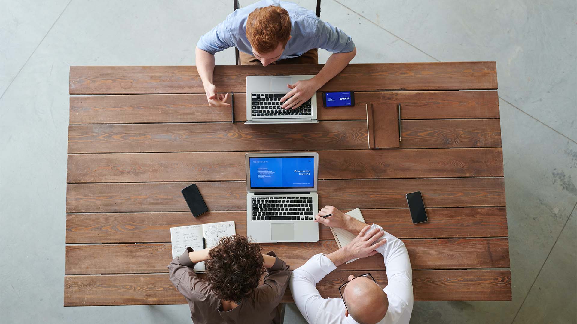 Photo vue du dessus d'un groupe de trois personnes travaillant sur une table en bois avec deux ordinateur portable